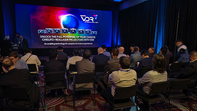 A group sits facing a large screen with images of projectors and text projected onto it. 