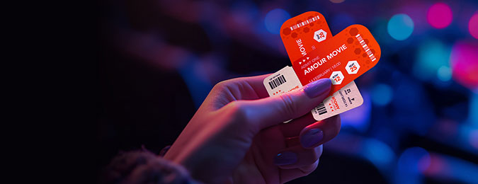 A hand holding two red movie tickets in a heart shape.